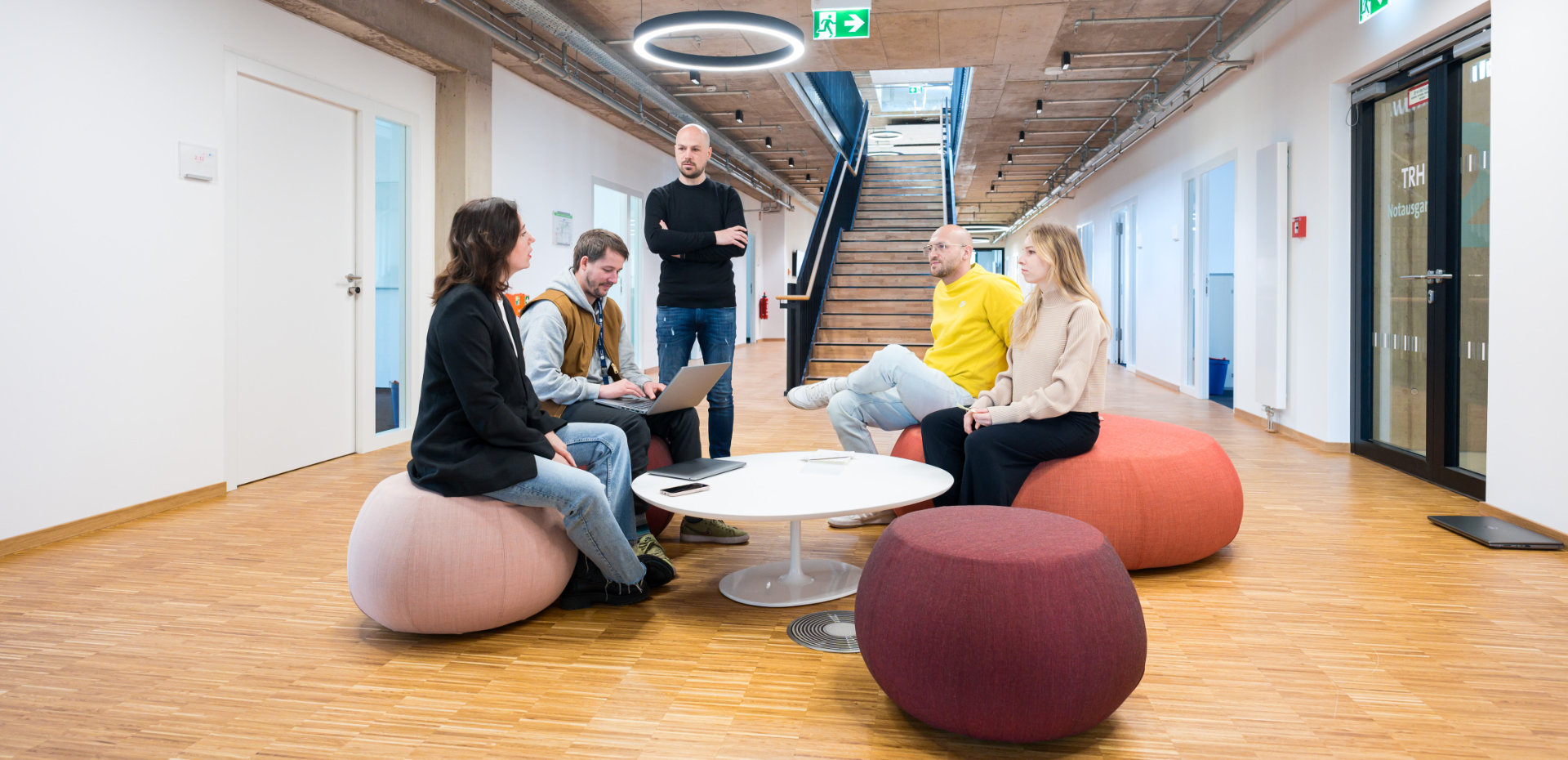 Eine Gruppe von fünf Menschen bespricht sich in einem großen Flur mit bunten Sitzmöbeln